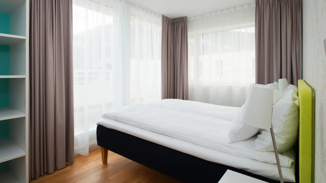 Dobbeltseng med med store vinduer og gardiner på Thon Hotel Sandven i Nordheimsund