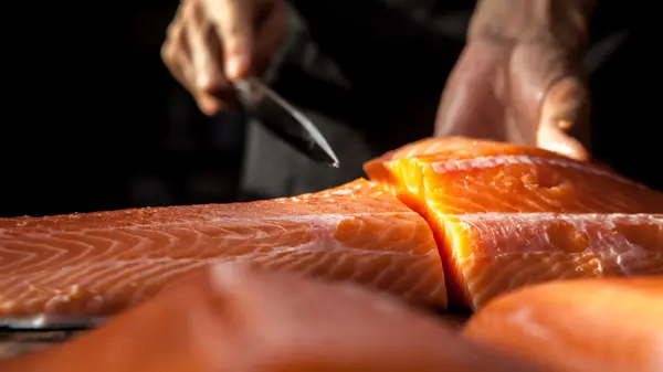 The big salmon is in the hands of the experienced Japanese chef.
He is using a knife to slice salmon fillet for sashimi and sushi.