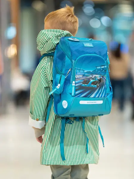 Gutt med ryggen til kamera i grønn jakke, bukse og blå skolesekk