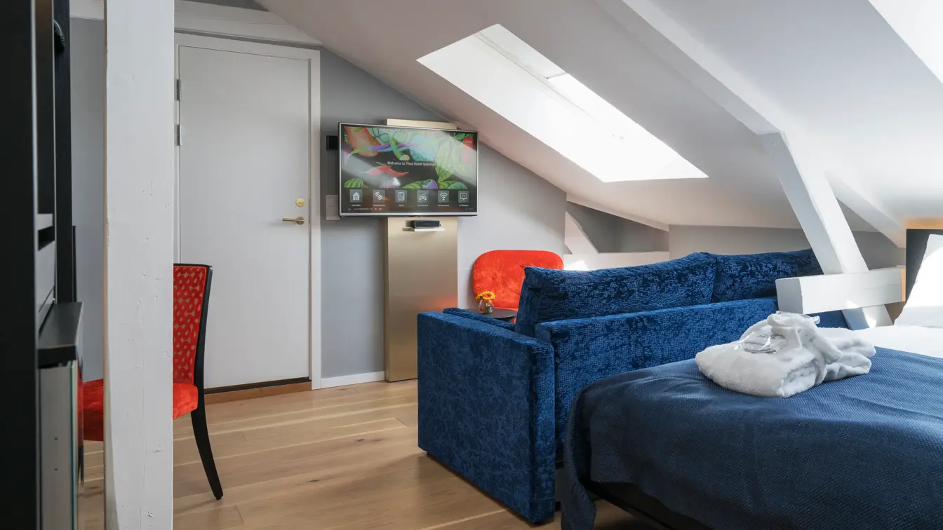 Sofa, dobbeltseng og tv på et rom med skråtak på buisness room på Thon Hotel Spectrum i Oslo sentrum
