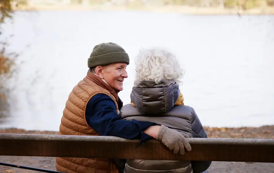 Eldre mann med lue sitter sammen med dame på en benk  