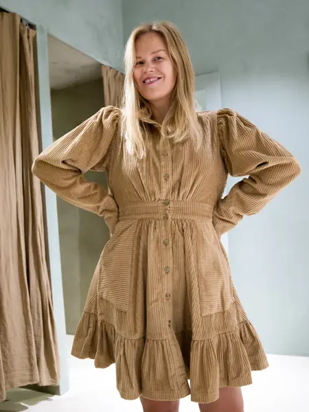 Jente med blondt hår, har på seg en knelang beige cordfløyelkjole