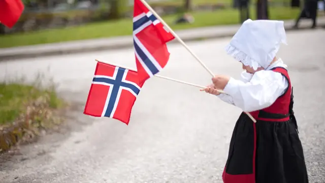 Jente i drakt feirer med to norgesflagg på 17. mai