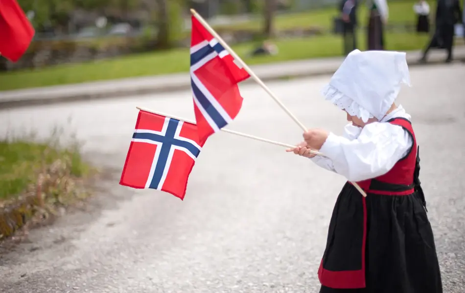 Jente i drakt feirer med to norgesflagg på 17. mai