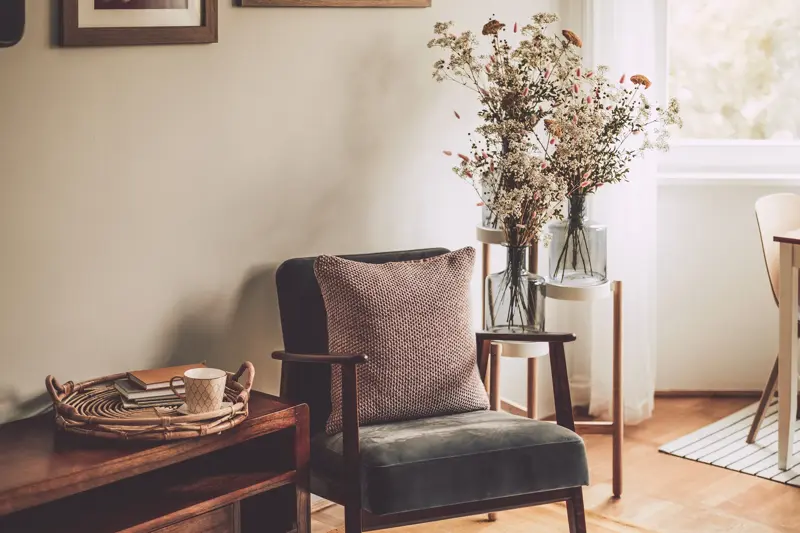 Nærbilde av stol med strikket pute ved siden av benk med kurv med kopp og bøker 