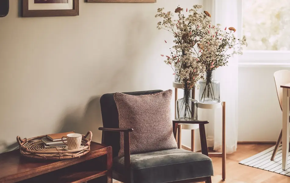 Nærbilde av stol med strikket pute ved siden av benk med kurv med kopp og bøker 