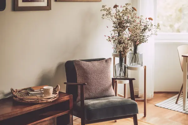 Nærbilde av stol med strikket pute ved siden av benk med kurv med kopp og bøker 