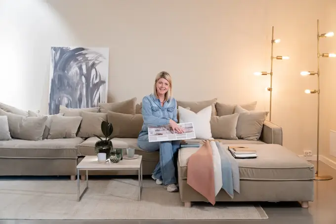 En dame som holder på med oppussing og tips om interiør trender for våren 2021. Damen har lyst halvlangt hå og har på seg en blå olaskjorte og blå olabukse. Fargene går i brunt og beige jordtoner og det er mye lilla og pastellfarger. Vårens interiør