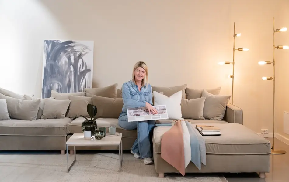 En dame som holder på med oppussing og tips om interiør trender for våren 2021. Damen har lyst halvlangt hå og har på seg en blå olaskjorte og blå olabukse. Fargene går i brunt og beige jordtoner og det er mye lilla og pastellfarger. Vårens interiør