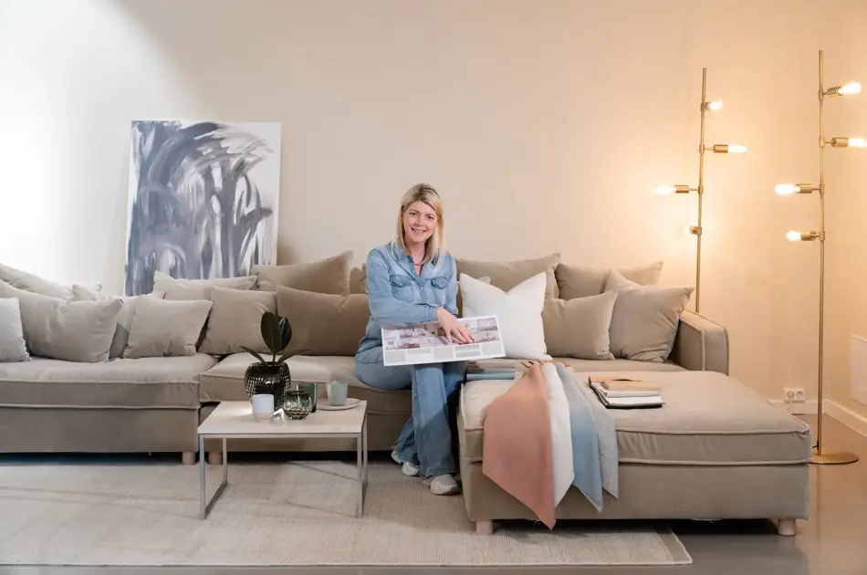 En dame som holder på med oppussing og tips om interiør trender for våren 2021. Damen har lyst halvlangt hå og har på seg en blå olaskjorte og blå olabukse. Fargene går i brunt og beige jordtoner og det er mye lilla og pastellfarger. Vårens interiør