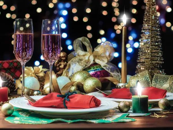 Bord som er pyntet til nyttårsfest, med røde servietter, julekuler, lys og to champagneglass. Foto til artikkel om hvordan du fikser nyttårsfest uten å slite deg helt ut.