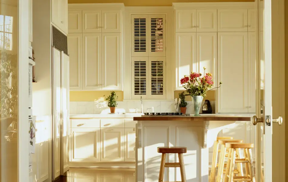Kjøkken med gule vegger og tak med hvite skapdører og trebenk med blomster på 