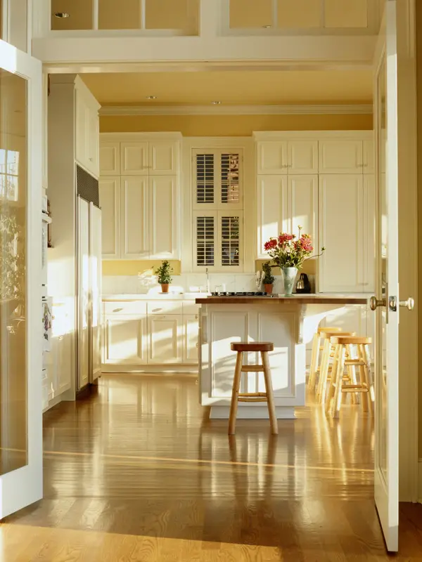 Kjøkken med gule vegger og tak med hvite skapdører og trebenk med blomster på 