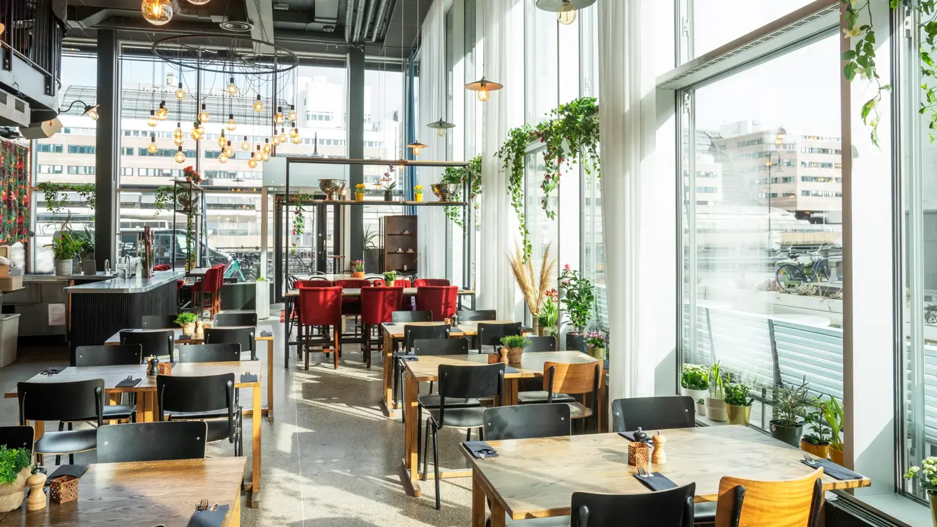 Retaurant med gulv-til-tak-vinduer på to sider, spisebord med fire eller seks tilhørende stoler, barddisk.