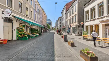 Handlegaten Torggata, sett fra øst til vest. Gågaten er pyntet med blomsterkasser og brostein. En grønnsakshandel på venstre side og restauranter med uteservering på høyre side.