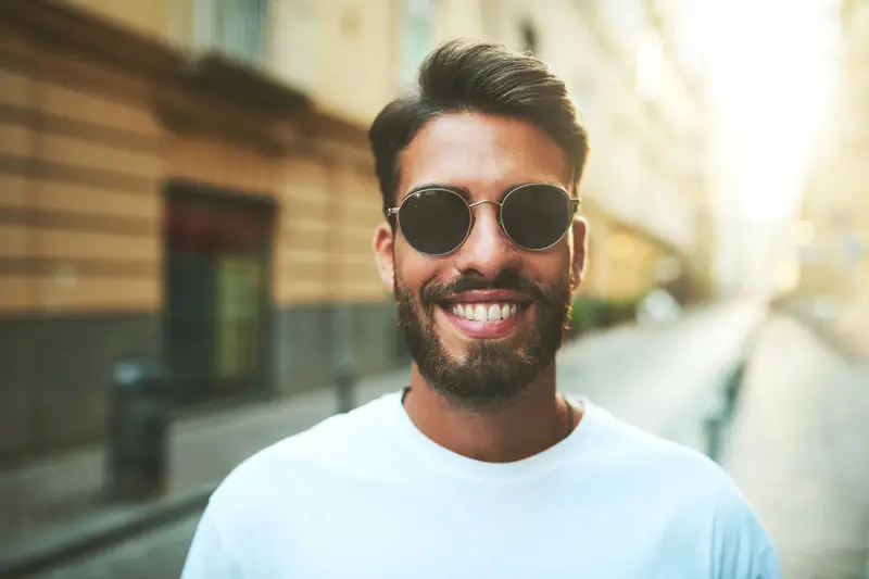 Mann med store runde solbriller smiler til kamera stående ute i en bygate