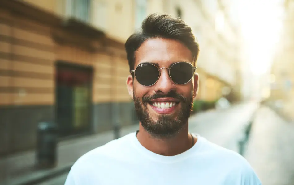 Mann med store runde solbriller smiler til kamera stående ute i en bygate