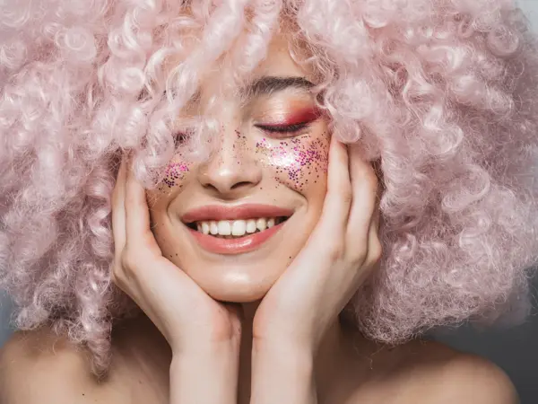 Modell med babyrosa afro og rosa glittersminke holder seg til ansiktet mens hun smiler og lukker øynene