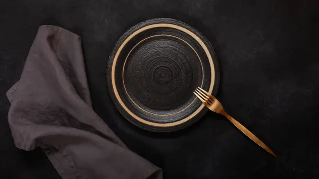 Empty ceramic plate and fork on black background