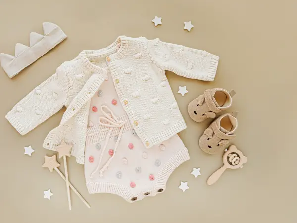 Pastel knitted romper with jumper, and shoes, cotton crown and toys. Set of baby clothes and accessories for little Princess on beige background.  Fashion newborn. Flat lay, top view