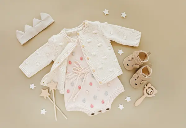 Pastel knitted romper with jumper, and shoes, cotton crown and toys. Set of baby clothes and accessories for little Princess on beige background.  Fashion newborn. Flat lay, top view