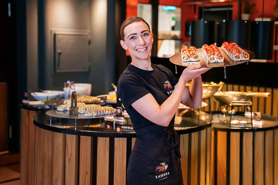 Ansatt som poserer med et brett sushi foran sushi buffeet