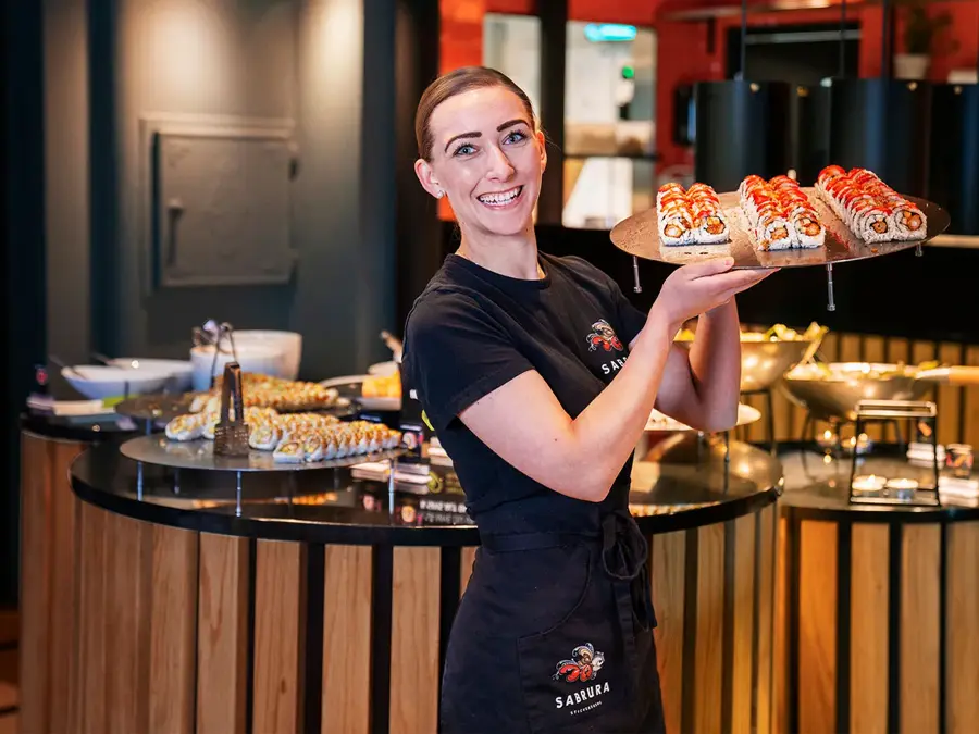 Ansatt som poserer med et brett sushi foran sushi buffeet
