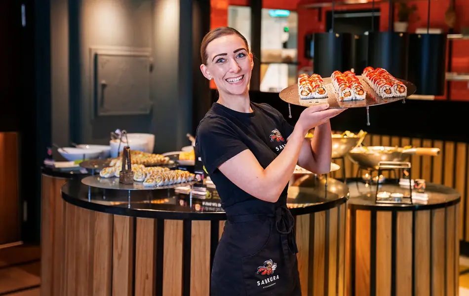 Ansatt som poserer med et brett sushi foran sushi buffeet