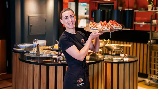 Ansatt som poserer med et brett sushi foran sushi buffeet