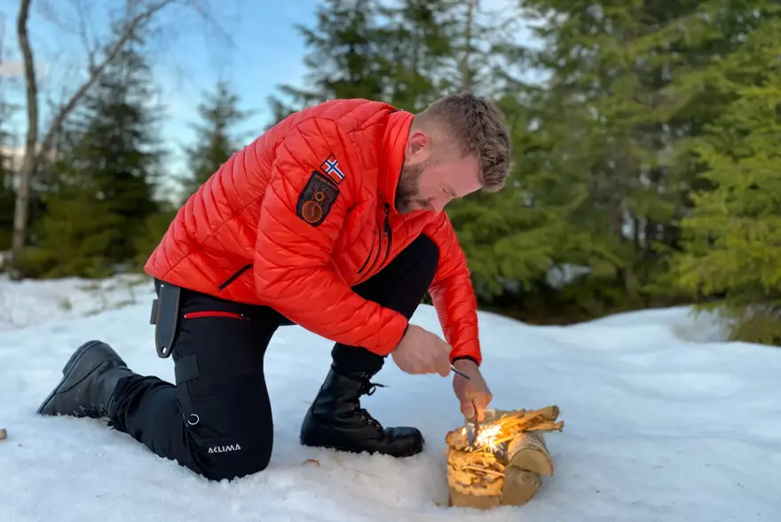 mann prøver å få fyr på et bål ute i fri natur