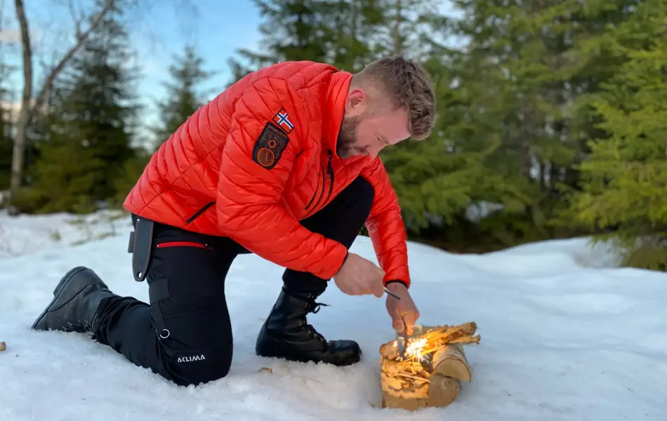 mann prøver å få fyr på et bål ute i fri natur