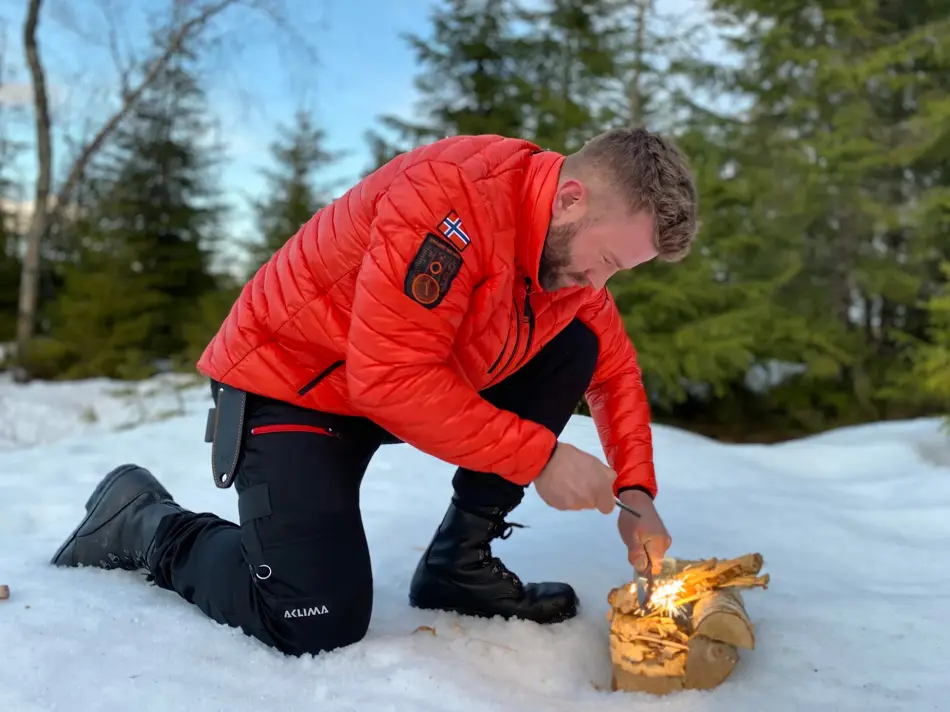 mann prøver å få fyr på et bål ute i fri natur