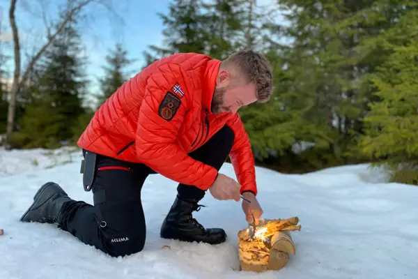 mann prøver å få fyr på et bål ute i fri natur