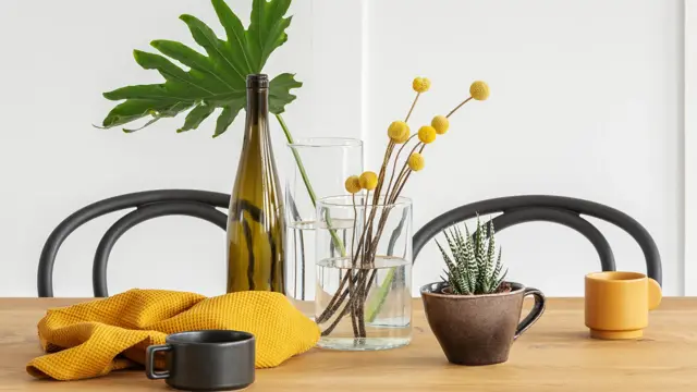Yellow flowers in glass vase, a bottle of wine, washcloth and coffee cup on wooden dining table