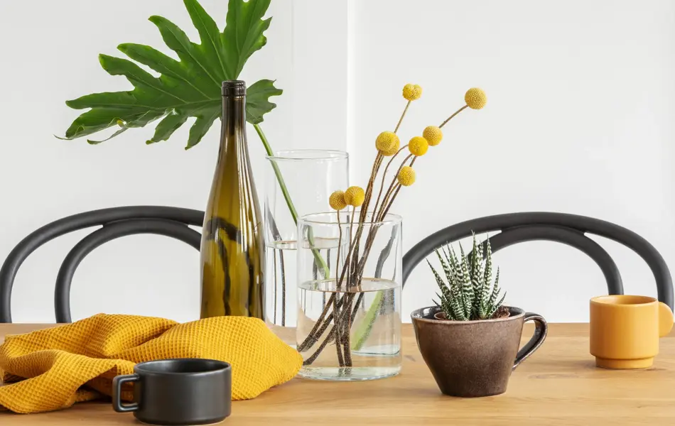 Yellow flowers in glass vase, a bottle of wine, washcloth and coffee cup on wooden dining table