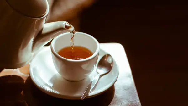 Pouring hot tea into white ceramic tea cup the time of tea break.