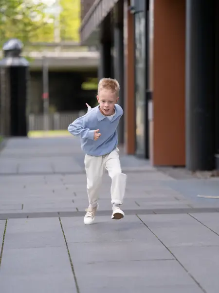 liten gutt løper ute i blå genser, hvit bukse og beige tøysko