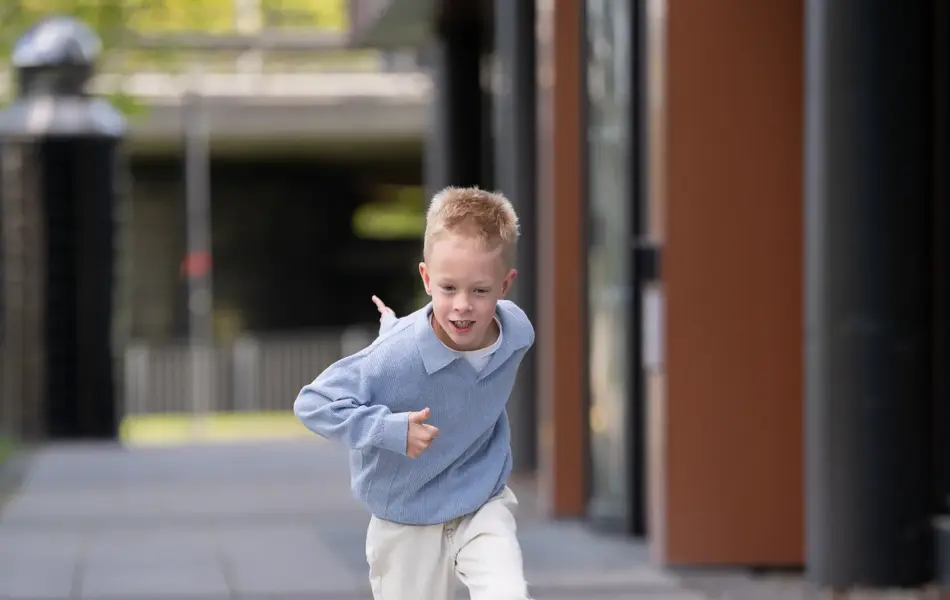 liten gutt løper ute i blå genser, hvit bukse og beige tøysko