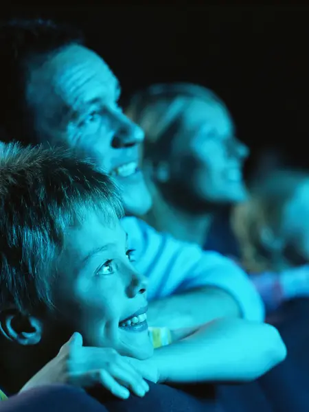 Gutt og mann sitter i mørk kinosal og blir lyst opp av blått lys. Foto til artikkel om opplevelsesgaver til farsdag.