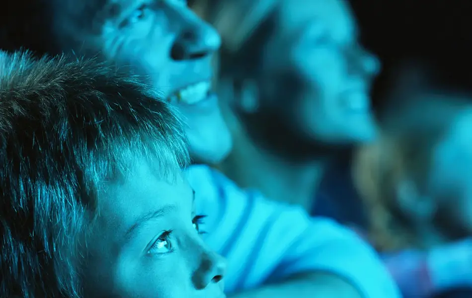 Gutt og mann sitter i mørk kinosal og blir lyst opp av blått lys. Foto til artikkel om opplevelsesgaver til farsdag.