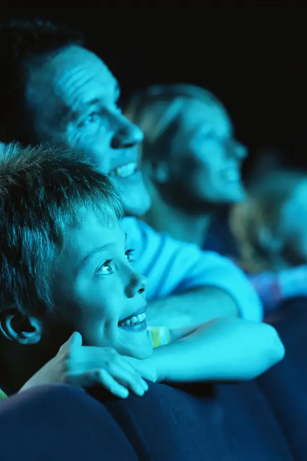 Gutt og mann sitter i mørk kinosal og blir lyst opp av blått lys. Foto til artikkel om opplevelsesgaver til farsdag.