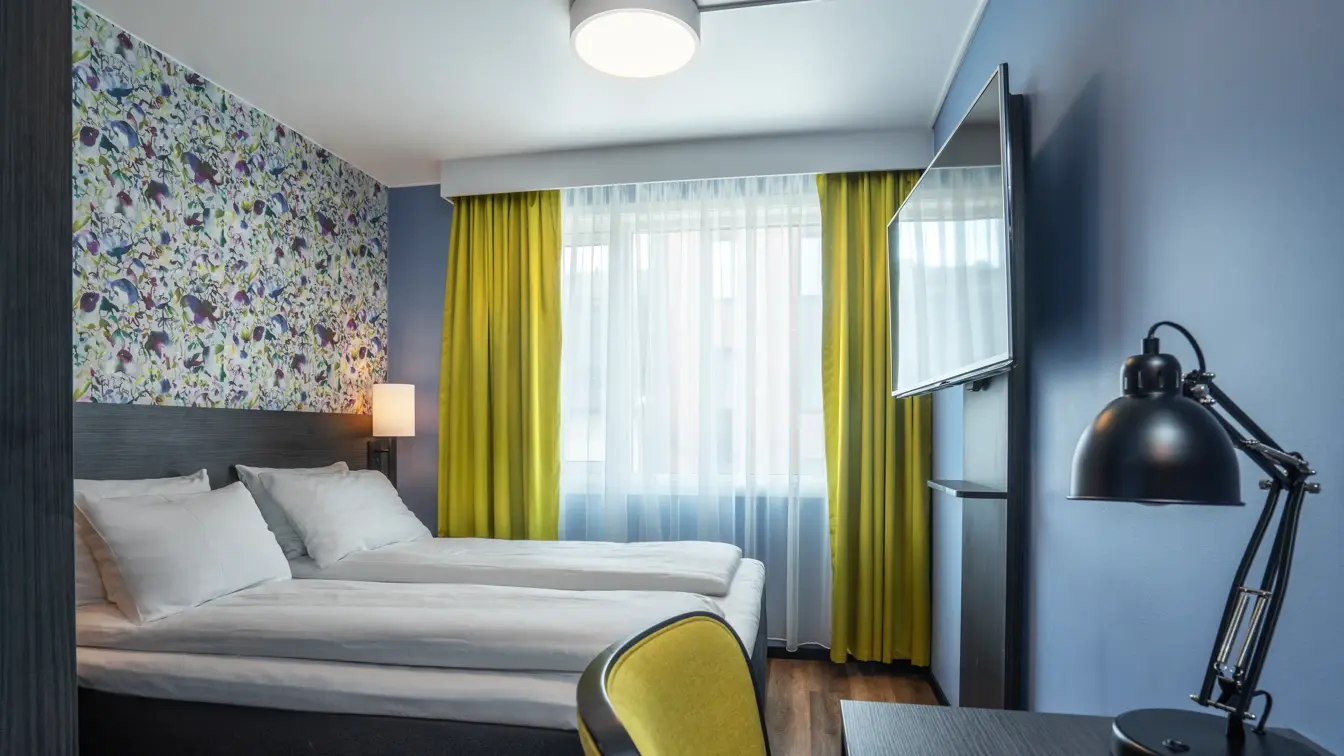 Tapetvegg, dobbeltseng, skrivebord, blå vegg, vindu, gule gardiner.