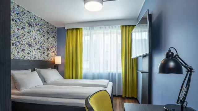 Tapetvegg, dobbeltseng, skrivebord, blå vegg, vindu, gule gardiner.