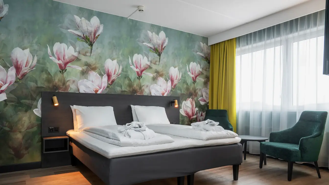 Blomstertapet, dobbeltseng, grønn lenestol, vindu, gule gardiner 