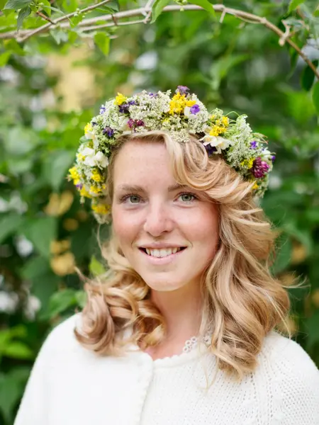 Blond jente smiler til kamera med blomsterkrans på hodet