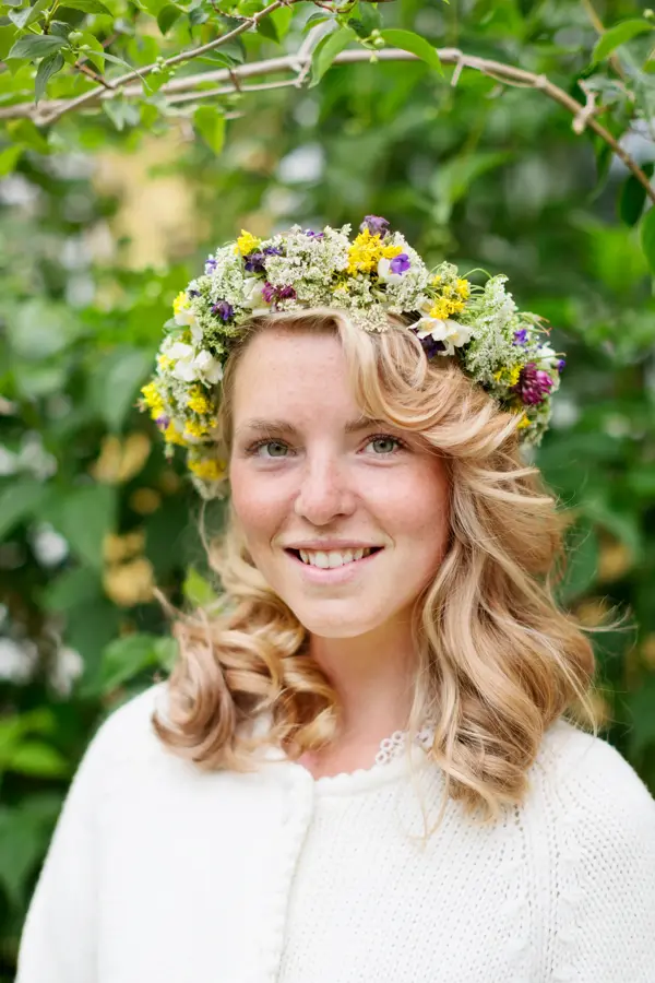 Blond jente smiler til kamera med blomsterkrans på hodet