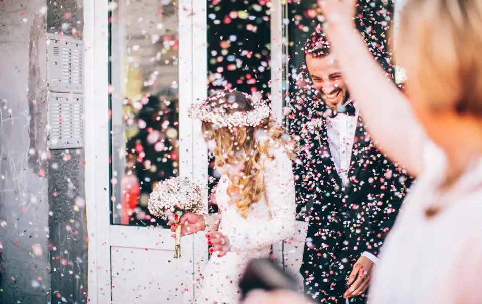 Photo of just married couple. Guests are throwing confetti in the air.