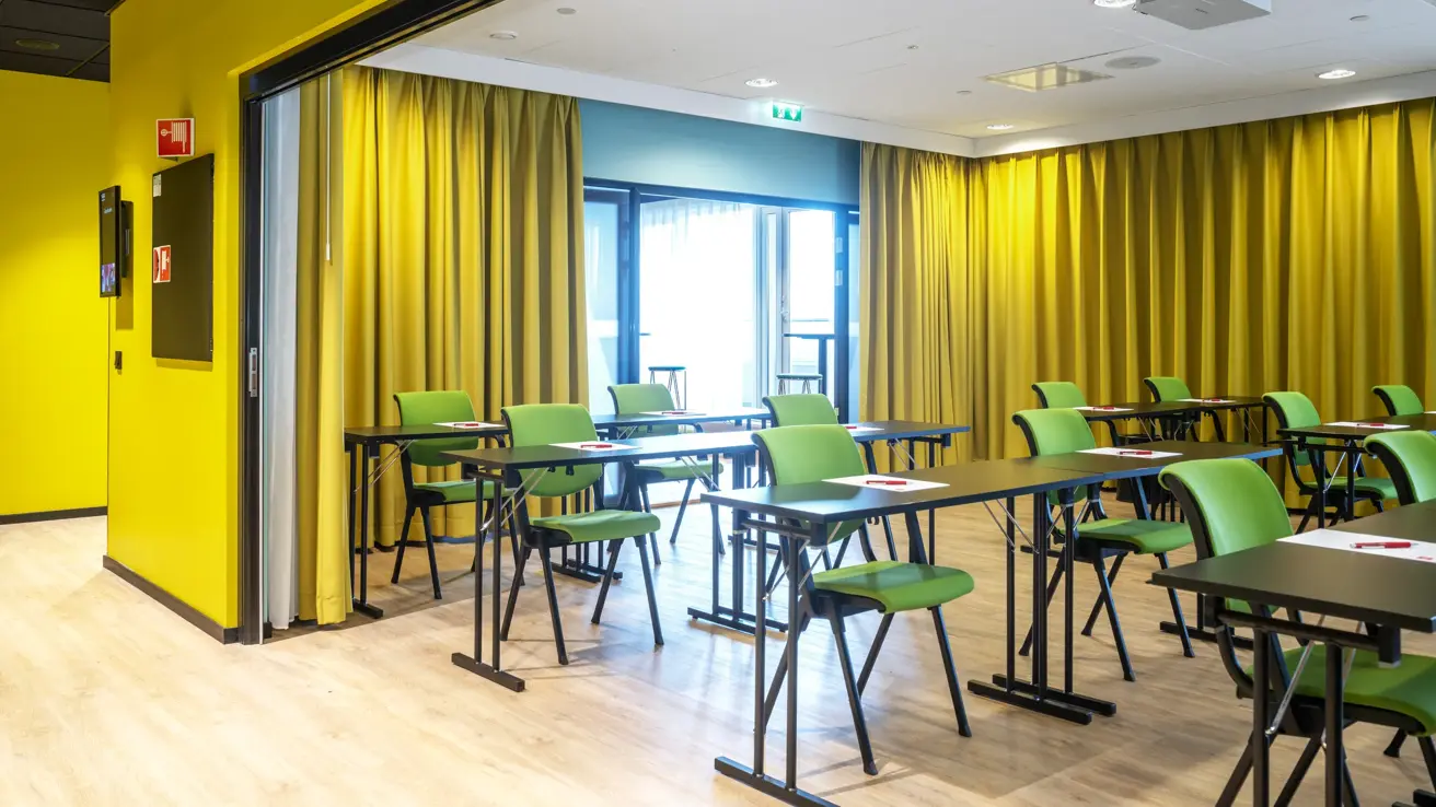 Konferanserom, klasseromoppsett, 1m avstand, grønne stoler, gulv vegg, gule gardiner. 