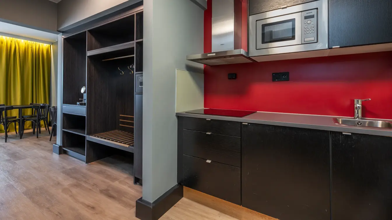 Business rom med kjøkkenkrok som inneholder mikrobølgovn, stekeplate, vifte, skap og vask. Åpen garderobeløsning og spisebord med stoler. 