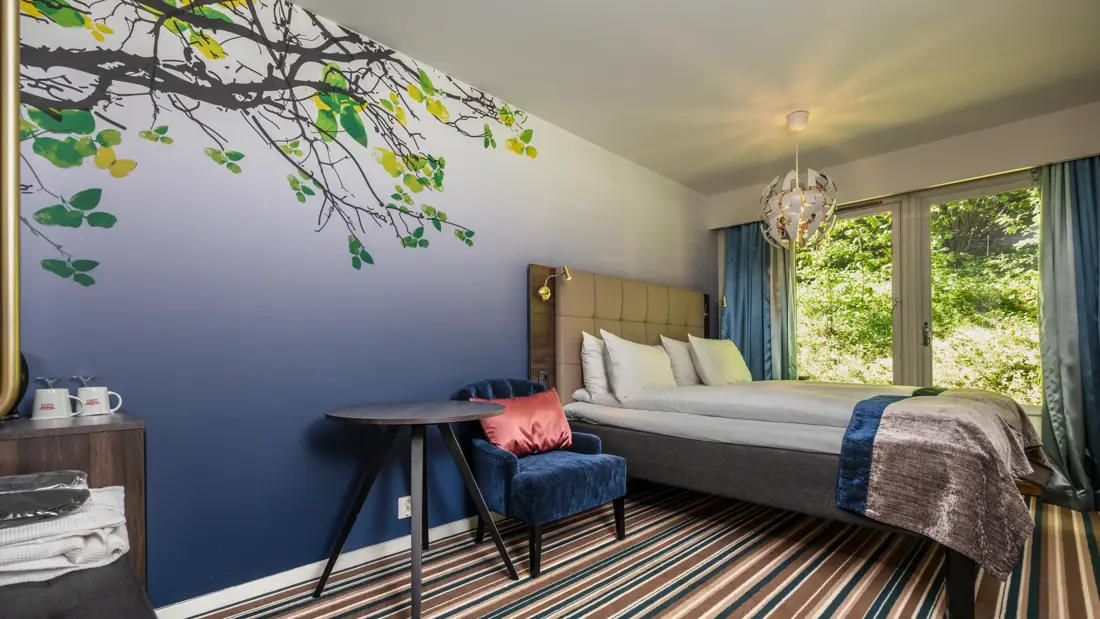 Superior rom med dobbeltseng, stripete gulvteppe, blå tapet, lysekrone over sengen, store vinduer og blå gardiner